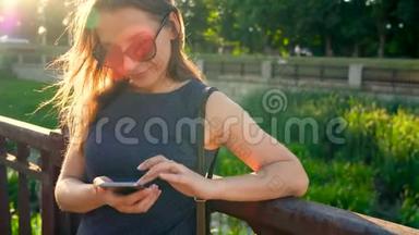 日落时分戴太阳镜的女人在户外使用智能手机