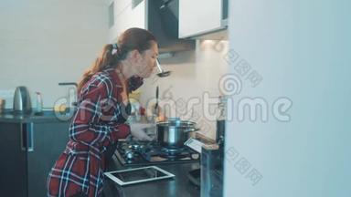 女人在厨房里煮汤锅，防止锅里的水，数码平板电脑上的食谱