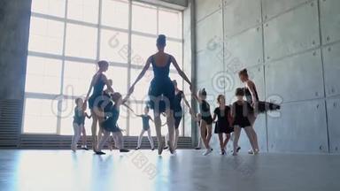 在芭蕾舞课上穿着黑色芭蕾舞裙的漂亮芭蕾舞演员。 可爱的女孩在芭蕾舞学校跳舞。 教师展示如何跳舞