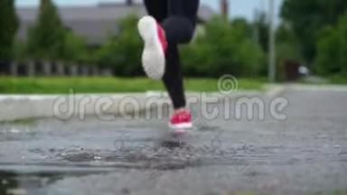 穿运动鞋的跑步者的腿。 运动女人在户外慢跑，<strong>踩</strong>在泥泞的水坑里。 单跑运动员在雨中奔跑