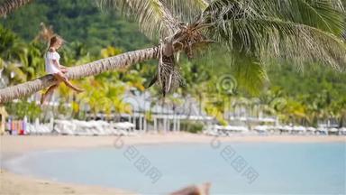 暑假期间坐在棕榈树上的热带海滩可爱的小女孩