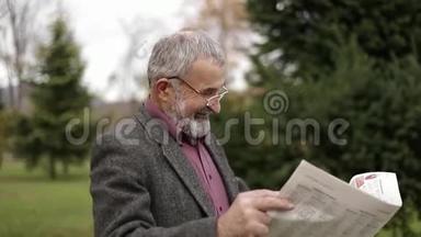 一位漂亮的祖父，留着漂亮的胡子，穿着灰色的夹克，在公园里看报纸