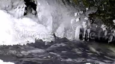 在山河清澈的冷水中冻住了雪白的大巨石.. 小冰柱闪烁在嘈杂的溪流的水晶水之上。