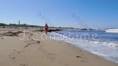 年轻的女人穿着红色的裙子在沙滩上奔跑，享受阳光，摆姿势。 泼水和风吹.. 慢动作