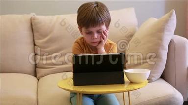 孩子在家里的床上使用平板电脑。 沙发上可爱的男孩正在看卡通，玩游戏，从笔记本电脑上学习。 教育、娱乐