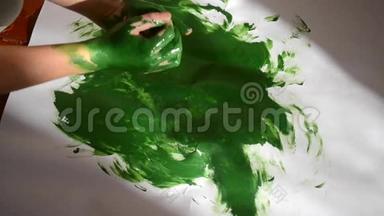 女孩把绿色的颜料涂在手上，画在纸上