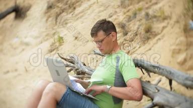 <strong>忙碌的</strong>、成熟<strong>的</strong>男人在一台手提电脑上<strong>工作</strong>，手里拿着打电话，坐在海滩上