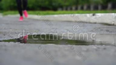 穿运动鞋的跑步者的腿。 运动女人在户外慢跑，踩在泥泞的水坑里。 单跑运动员在雨中奔跑
