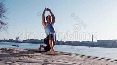 年轻的白种人通过在平静的河流附近的海滩上练习瑜伽健身运动放松<strong>身心</strong>，背景是城市
