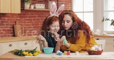 复活节快乐。 妈妈和她的小女儿正在准备复活节。 幸福的家庭在舒适的厨房里画复活节彩蛋