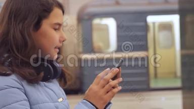 十几岁的女孩带着智能手机和耳机等待地铁，很多人聚集在地下。 地下地铁公司