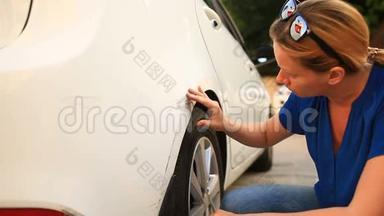 看着一辆损坏的车。 一位金发女子在车祸后检查汽车损坏