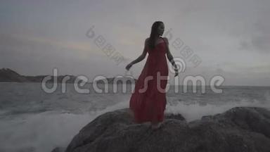 美丽迷人的女人穿着红裙子，在海边的岩石上尽情享受