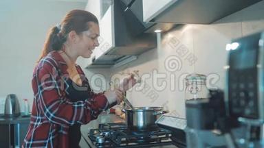女人在厨房<strong>煮汤</strong>锅，防止锅里的水，看看数字平板上的食谱。 妇女