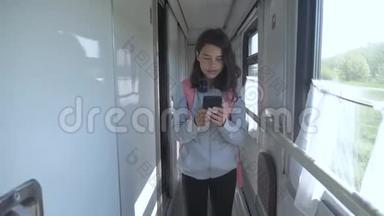 十几岁的女孩带着背包和智能手机在火车车厢里散步。 旅游生活方式运输铁路