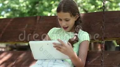有平板电脑的漂亮女孩坐在秋千凳上