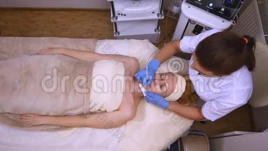 年轻的美女躺在临床桌上，美容师给她做了面部电刺激按摩