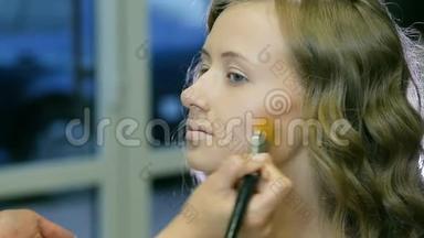专业化妆师在金色卷发和蓝眼睛模型皮肤上涂上色调霜。