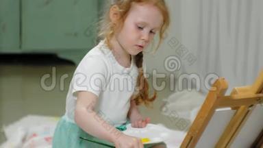 漂亮的红发女孩坐在画架前面的画室的地板上，<strong>画画笔</strong>和彩色颜料