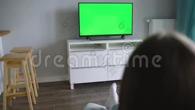 女人坐在椅子上，用绿色的屏幕看<strong>电视</strong>，用<strong>遥控器</strong>切换频道。 铬键