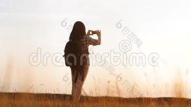 hipsterhiker剪影女孩正在手机智能手机上拍摄美丽自然日落的视频