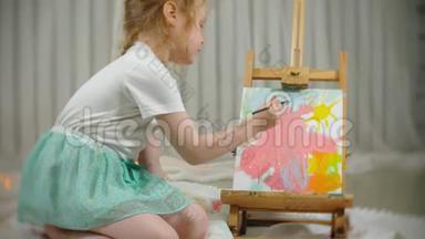 漂亮的红发女孩坐在画架前面的画室的地板上，<strong>画画笔</strong>和<strong>彩</strong>色颜料