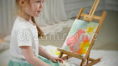 漂亮的红发女孩坐在画架前面的画室的地板上，<strong>画画笔</strong>和彩色颜料