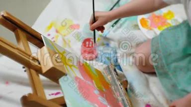 漂亮的红发女孩坐在画架前面的画室的地板上，画画笔和彩色颜料