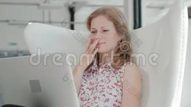 漂亮的女商人坐在玻璃办公室的白色椅子上，在笔记本电脑后面工作