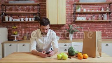 男人在家厨房用<strong>手机浏览</strong>。 英俊的年轻人在智能手机上浏览，微笑着快乐。