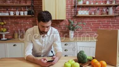 男人在家厨房用<strong>手机浏览</strong>。 英俊的年轻人在智能手机上浏览，微笑着快乐。