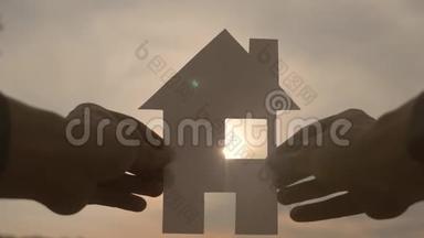 幸福家园建设理念.. 在日落的剪影阳光下，一个人手里拿着一个纸房子。 生活