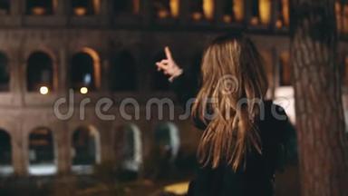 慢点。 年轻漂亮的女人回头看镜头，<strong>用手指</strong>在意大利罗马的竞技场上展示。