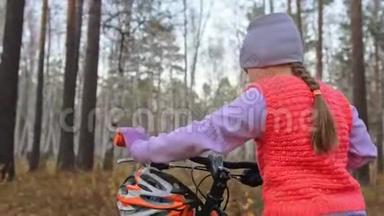 一个高加索儿童在秋天公园骑自行车走路。 小女孩在森林里走着黑色的橙色循环。 孩子是干的