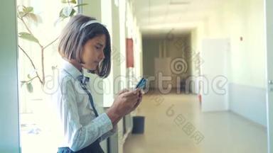 在学校概念上使用智能手机的女学生教育。 年轻的女孩，用智能手机站在窗户旁边