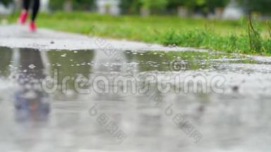 穿运动鞋的跑步者的腿。 运动女人在户外慢跑，<strong>踩</strong>在泥泞的水坑里。 单跑运动员在雨中奔跑