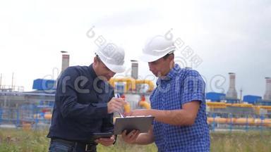团队合作。 工业生活方式煤气生产站的概念。 慢动作视频。 两名戴头盔的工程师正在学习