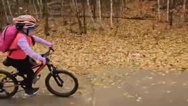 一个高加索儿童在秋季公园骑自行车。 小女孩骑着黑色橙色的自行车在森林里。 孩子是干的