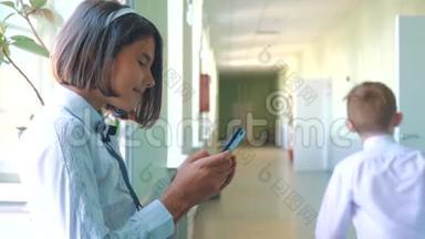在学校概念上使用智能手机的女学生教育。 十几岁的小女孩，用智能手机站在窗口