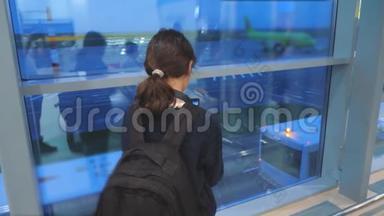女儿带背包飞机飞行机场概念。 带着智能手机的少女望着窗外