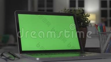 带有绿色屏幕的笔记本电脑。 黑暗的办公室。 完美地放置你自己的图像或视频。