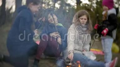 旅途中游客的幸福家庭。 妈妈和孩子们在帐篷附近的火上煎棉花糖
