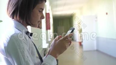 在学校概念上使用智能手机的女学生教育。 十几岁的小女孩，用智能手机站在窗口