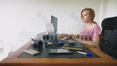 漂亮的年轻女<strong>人坐</strong>在办公桌<strong>前</strong>，一边用笔记本<strong>电脑</strong>和<strong>电脑</strong>工作。