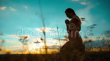 女孩在日落时双手交叉祈祷剪影。 慢动作录像。 女孩双手交叉祈祷祈求上帝