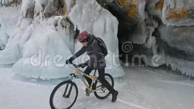 人正骑自行车在冰窟附近。 有冰洞和冰柱的岩石非常美丽。 骑自行车的人穿着