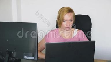 漂亮的年轻女<strong>人坐</strong>在办公桌<strong>前</strong>，一边用笔记本<strong>电脑</strong>和<strong>电脑</strong>工作。