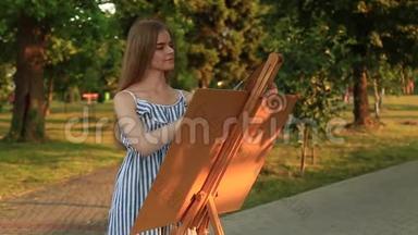 美丽的女孩在公园里画一幅画，用颜料和铲子调<strong>色板</strong>。 带有<strong>图片</strong>的简易帆布