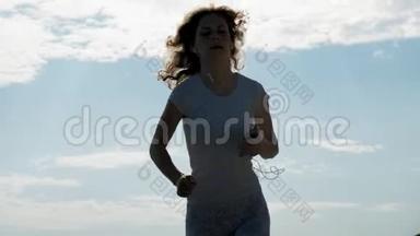 一个身材好的年轻女子在黎明时在海里从事体操。 她戴着耳机沿着海岸跑