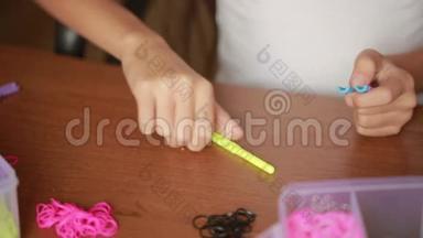 小女孩编织橡皮筋的腕带。 编织的彩色橡皮筋